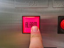 دکمه آلارم در آسانسور. متن برجسته برای افراد نابینا وجود دارد